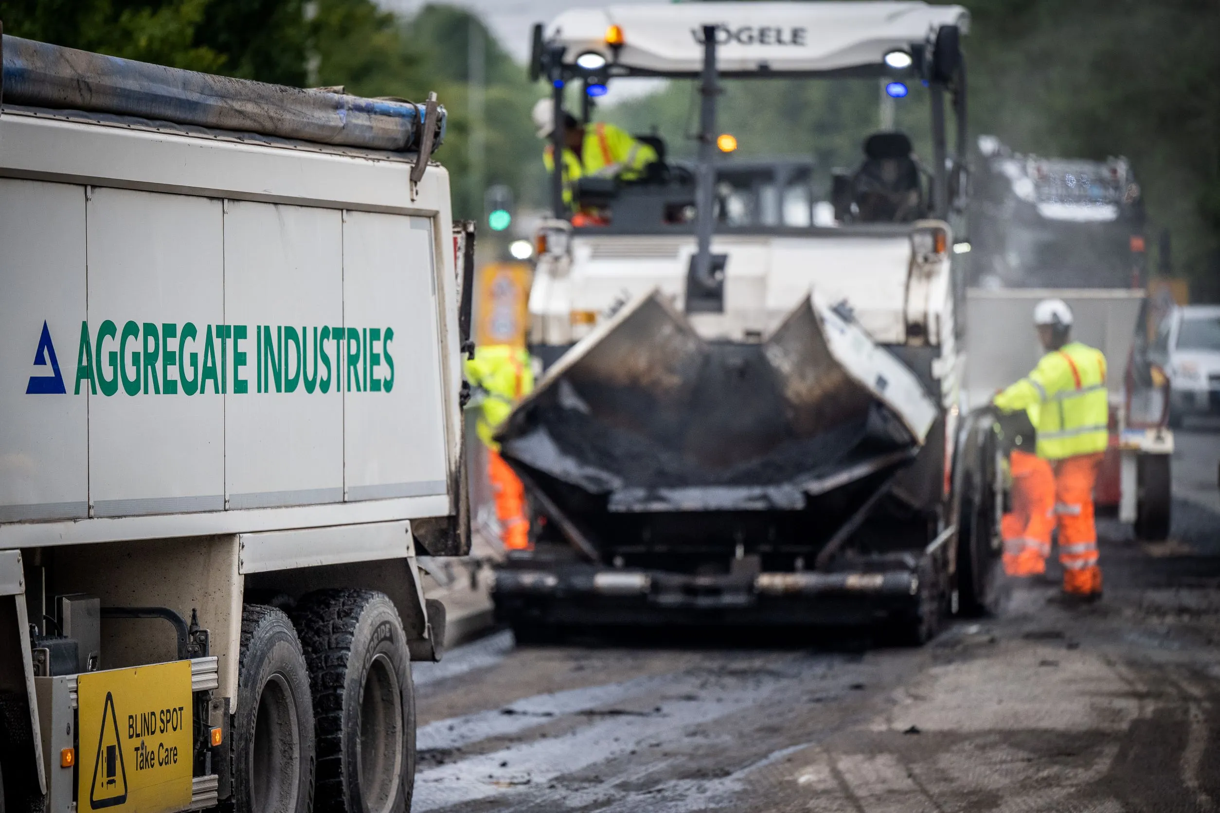 An Aggregate Industries lorry and paver resurfacing a road.