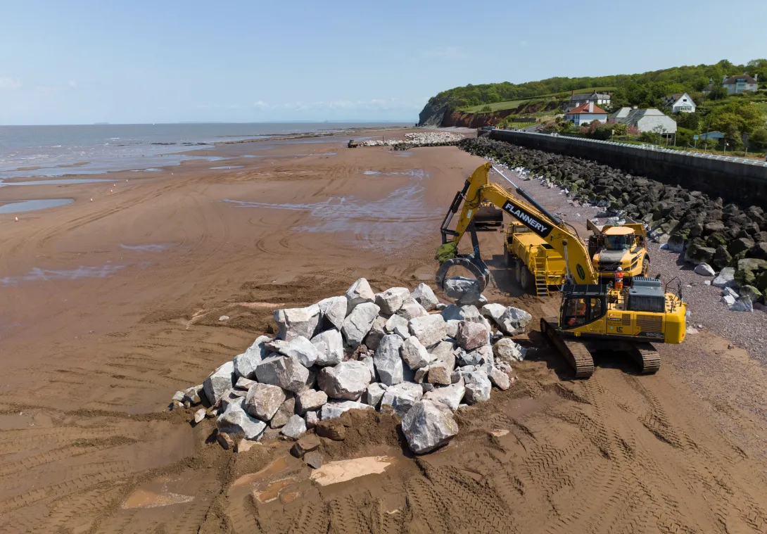 A pile of Armourstone granite boulders on Blue Anchor beach Somerset with a digger. It is part of coastal defence work.