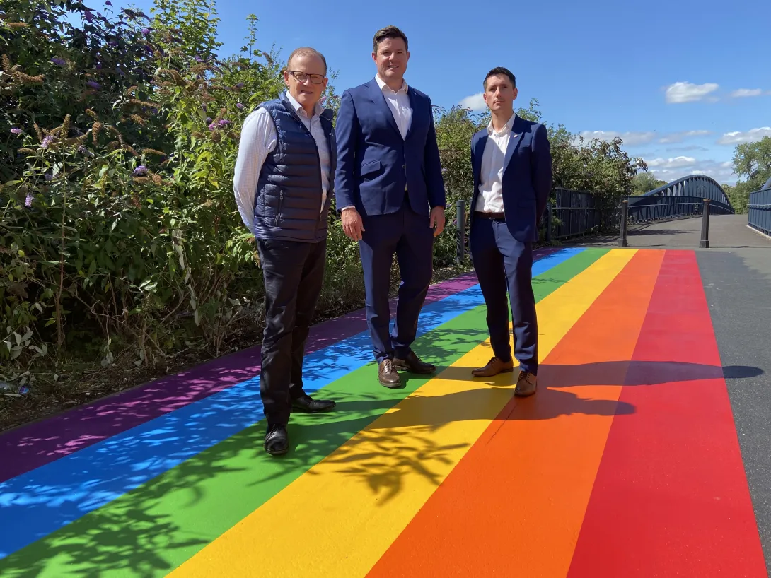 Hr Director James Roberts, Surfacing Solutions Managing Director Tom Edgcumbe and High Viz LGBTQ+ Network Lead Aron Simpson-Webb stand on a new Pride themed pathway on the way into Leicester Pride at Abbey Park